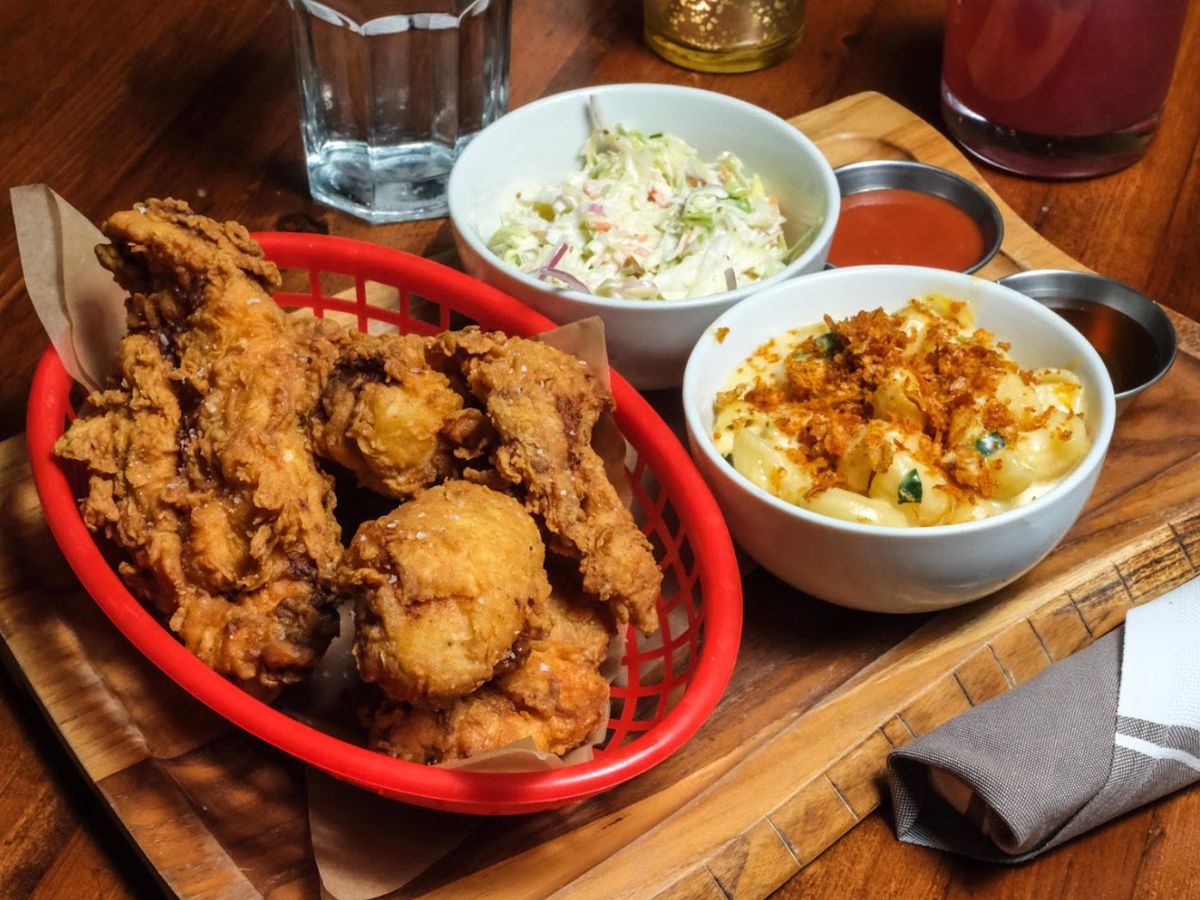 A basket of fried chicken next to a bowl of mac ânâ cheese and a bowl of cole slaw.