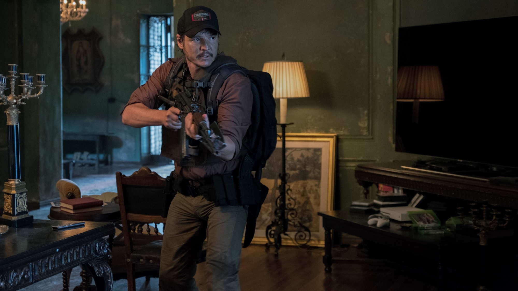 An armed man stands in a barren dining room.
