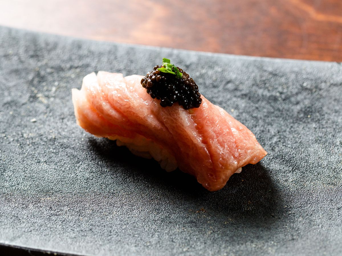Black caviar delicately placed on top of a pink slice of fatty tuna sushi.