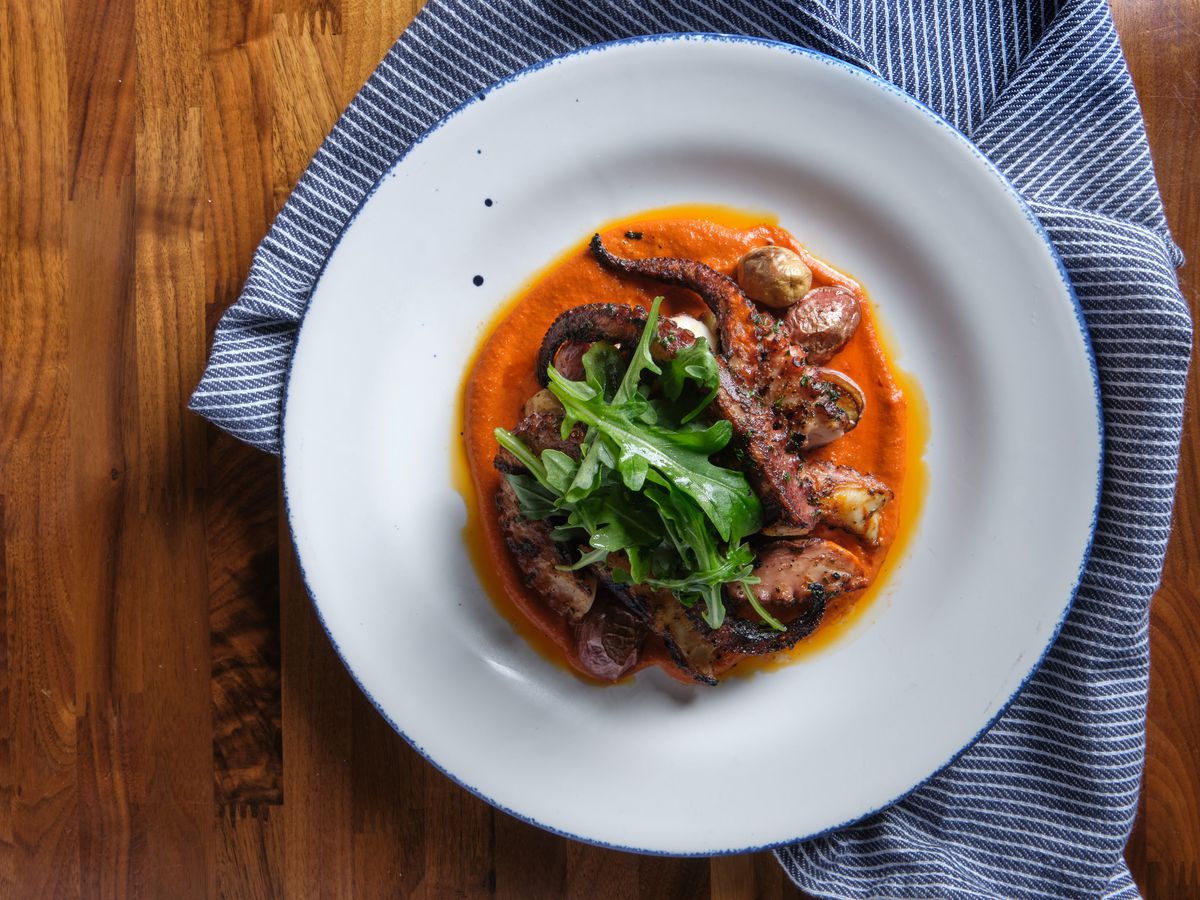 Grilled octopus in a white bowl with a blue towel and wood table under.