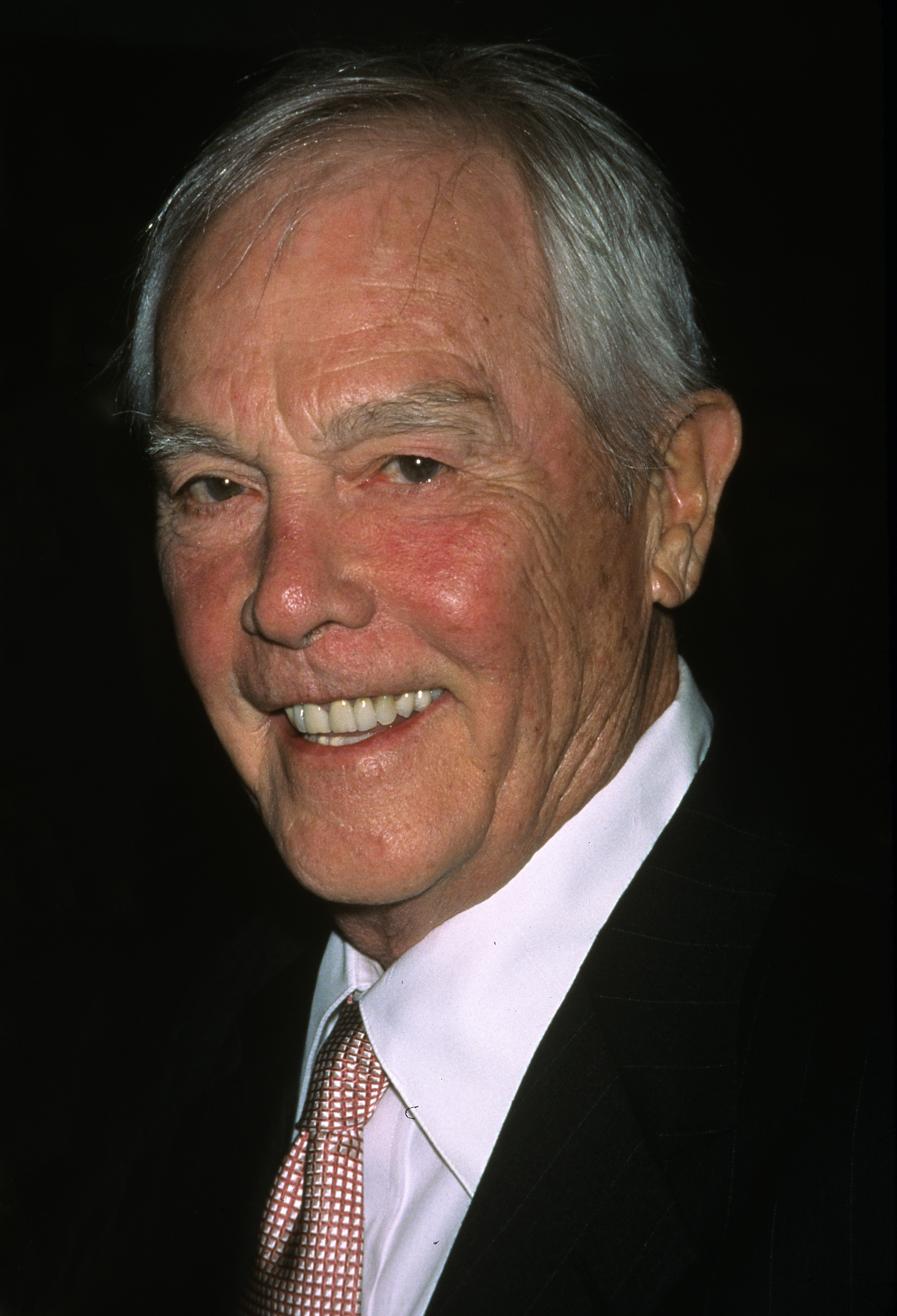 Harry Connick Sr. smiles while wearing a suit and tie.