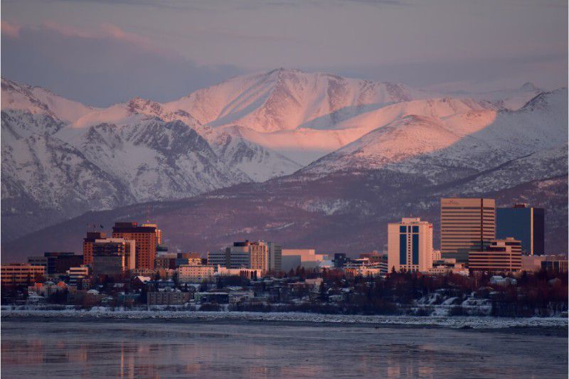 Mountains glowing at sunrise pink in Anchorage Alaksa with city and sea in foreground