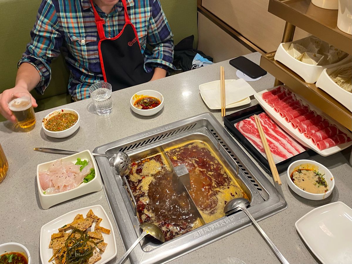 Raw meats, seafood, and vegetables displayed on a table next to two bubbling pots of broth.