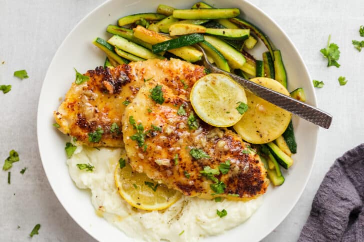 Easy 30-minute Chicken Lemon on a plate with mashed potatoes and zucchini topped with lemon butter.