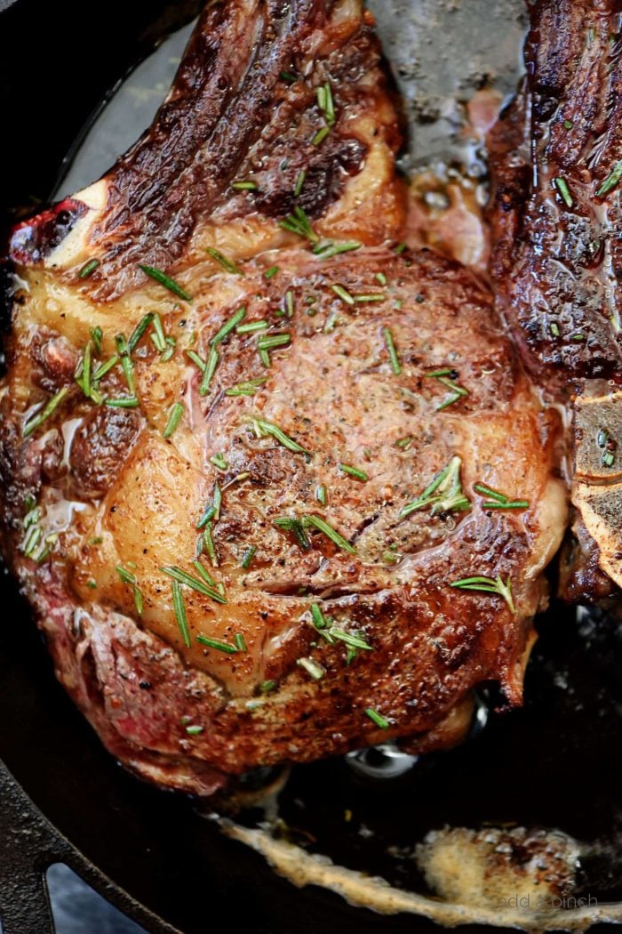 Butter-basting a steak topped with rosemary with a stainless spoon in a skillet // addapinch.com