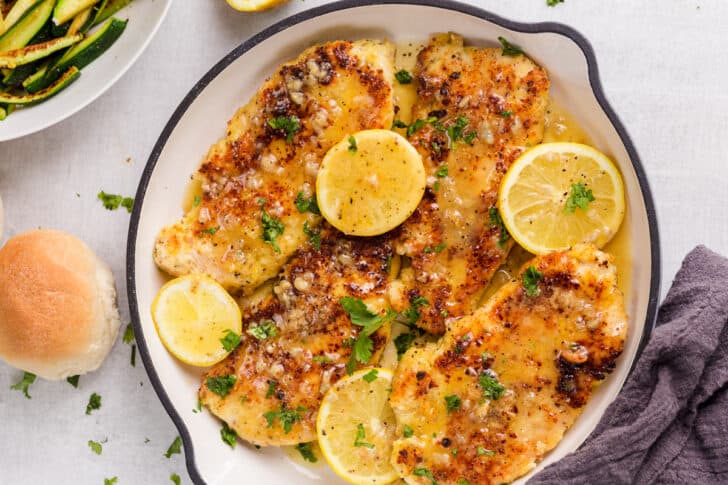 Parmesan crusted chicken with a lemon butter sauce in a skillet topped lemon slices.